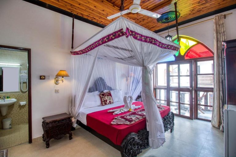 Habitación con cama de dosel y mosquitera en Tembo House Hotel, decoración exótica con ventana de colores