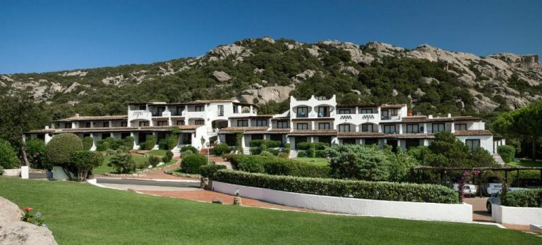 Vista exterior del Hotel La Bisaccia con jardines y montaña rocosa de fondo en Cerdeña
