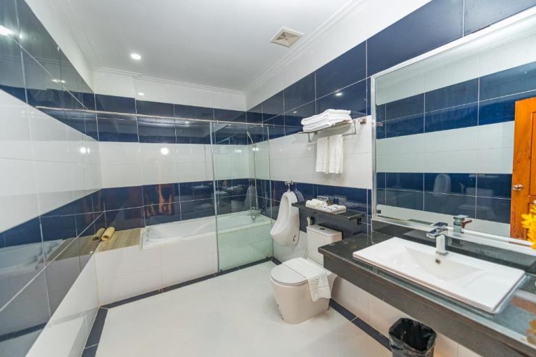 Baño completo con bañera y ducha acristalada en Kampong Thom Royal Hotel, azulejos azules y blancos