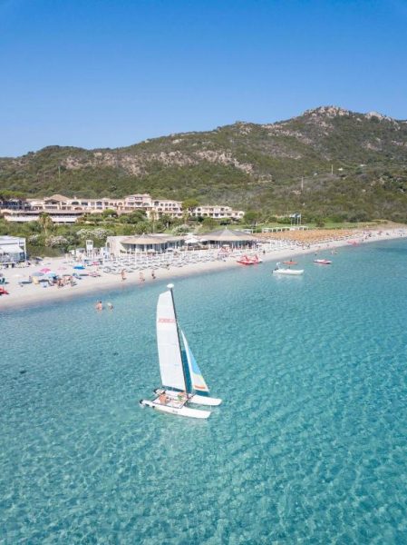 Playa de aguas cristalinas con catamarán del Abi d'Oru Sardinian Beach Resort & Spa en Cerdeña