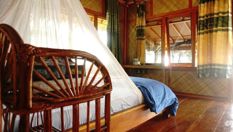 Habitación con cama doble, mosquitera y decoración de bambú natural en Ricky's Beach House