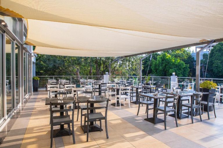 Terraza restaurante exterior con mesas y sillas del hotel Mayfair Gardens rodeada de vegetación