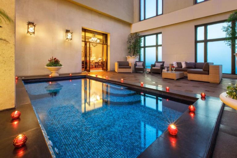 Piscina interior con velas románticas y zona lounge en The Leela Palace New Delhi