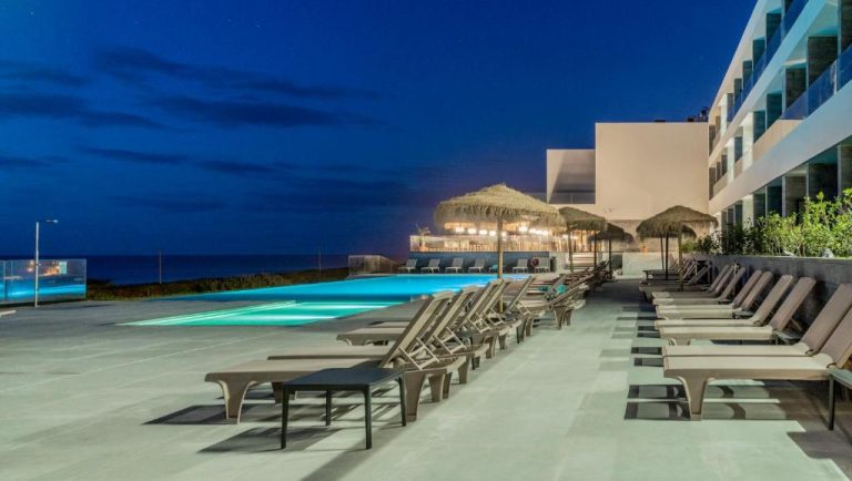Piscina exterior iluminada de noche con tumbonas y bar de playa en Hotel Verde Mar & SPA