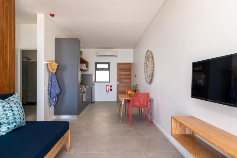 Salón comedor con cocina equipada y sillas rojas en apartamento del hotel La Desirade
