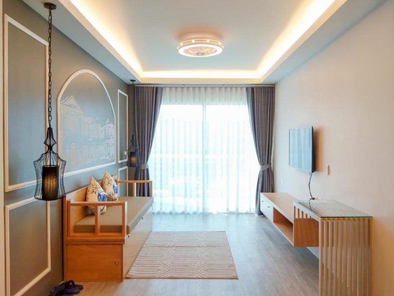 Salón luminoso con decoración asiática y TV mural en Peranakan House, con ventanal y mobiliario de madera