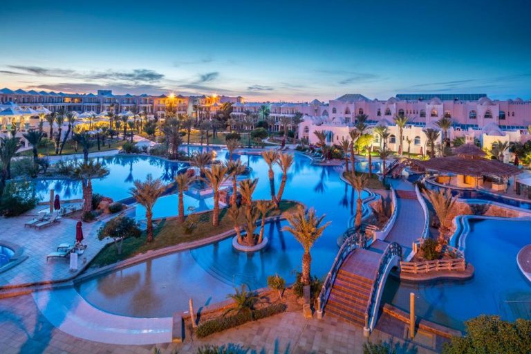Vista aérea de las piscinas exteriores iluminadas del Hasdrubal Prestige Thalassa & Spa Djerba al atardecer
