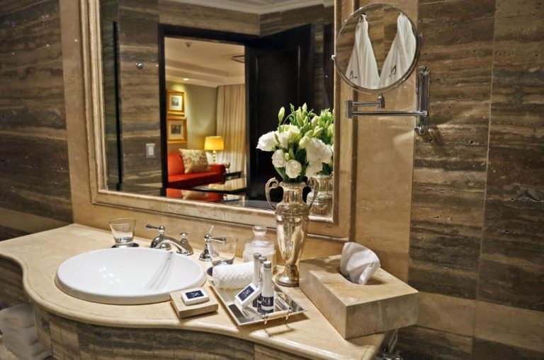 Lujoso baño con lavabo de mármol, flores blancas y amenities en Nino Hotel Boutique