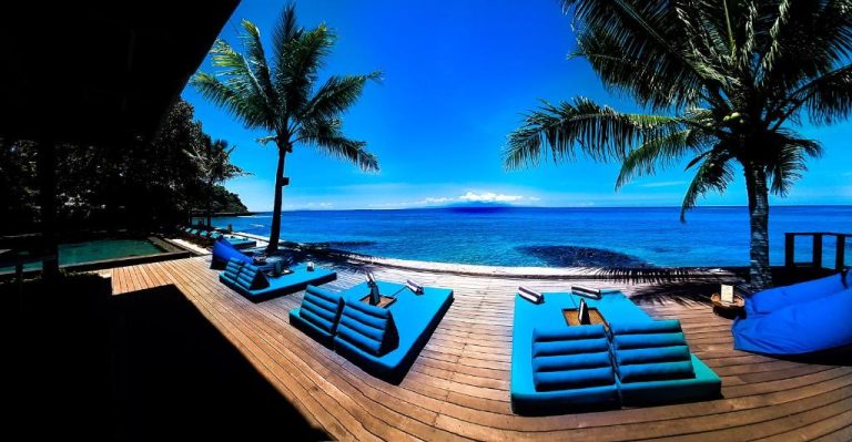 Terraza con tumbonas azules y piscina infinita frente al mar en Jeeva Santai Villas