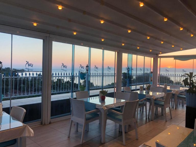 Restaurante con vistas al mar al atardecer en el Aura Boutique Hotel, con mesas y sillas blancas
