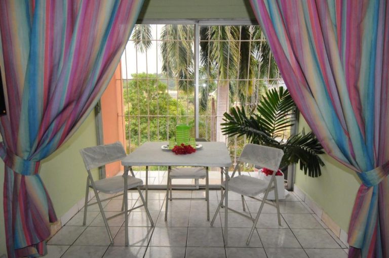 Comedor con mesa y sillas blancas en terraza interior con cortinas de colores del Verney House Resort