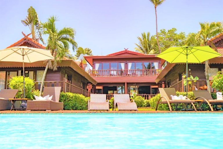 Piscina exterior con tumbonas y sombrillas del Erawan Villa Hotel rodeado de palmeras tropicales
