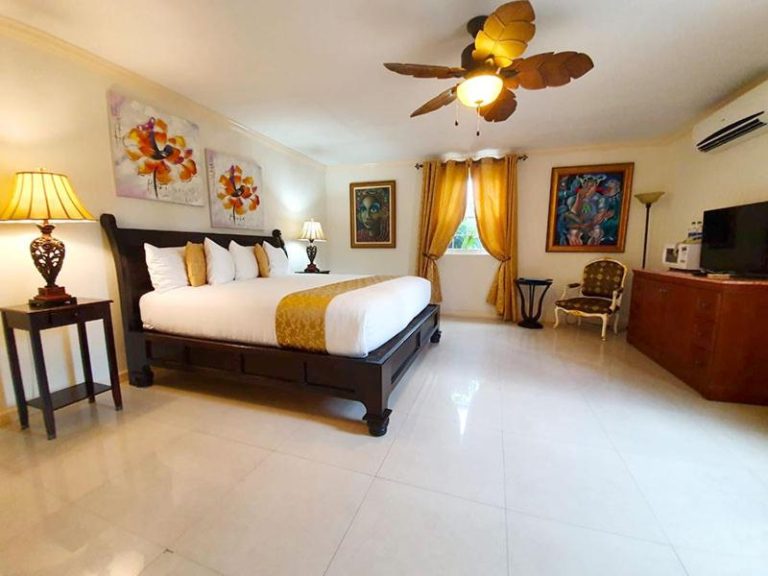 Habitación King con cama de madera oscura, ventilador de techo y decoración tropical en Ocean West Boutique Hotel