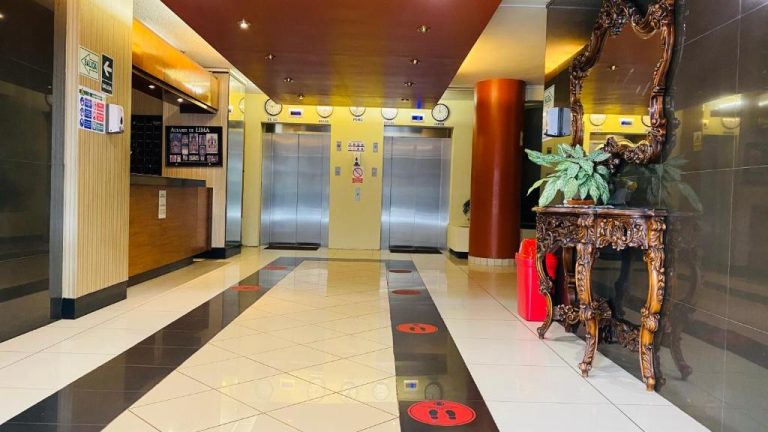 Lobby del Hotel Continental Lima con ascensores de acero, columna decorativa y mesa tallada con planta