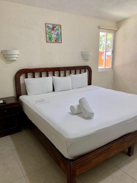 Habitación doble con cama matrimonial de madera y ropa de cama blanca en Hotel Caribe