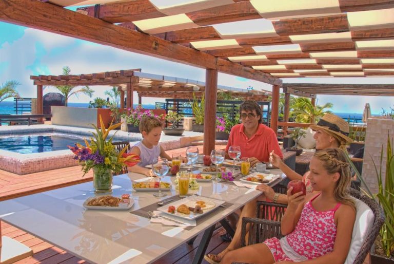 Familia disfrutando del desayuno en la terraza con piscina y vista al mar en La Divina by Aldea Thai