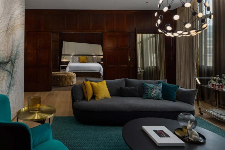 Suite de lujo del QT Sydney con salón moderno, sofá gris y acceso al dormitorio con paneles de madera