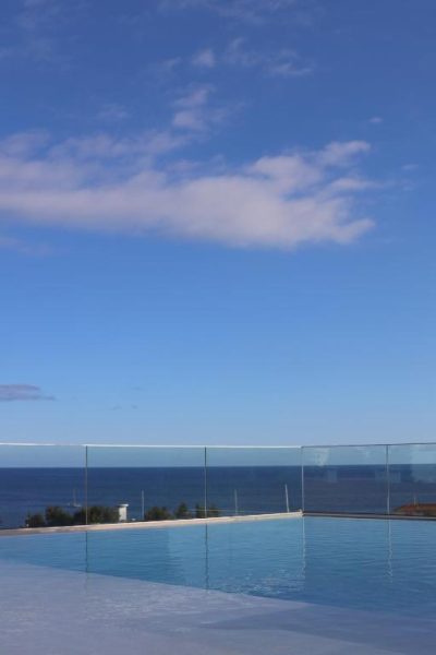 Piscina infinita con vistas al mar del Three House Hotel y barandilla de cristal bajo cielo azul