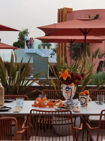Terraza exterior del Three House Hotel con mesas decoradas, sombrillas rojas y plantas tropicales