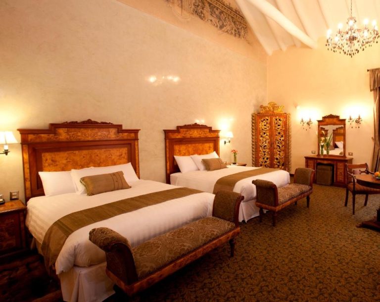 Habitación doble de lujo con decoración colonial y araña de cristal en Aranwa Cusco Boutique Hotel