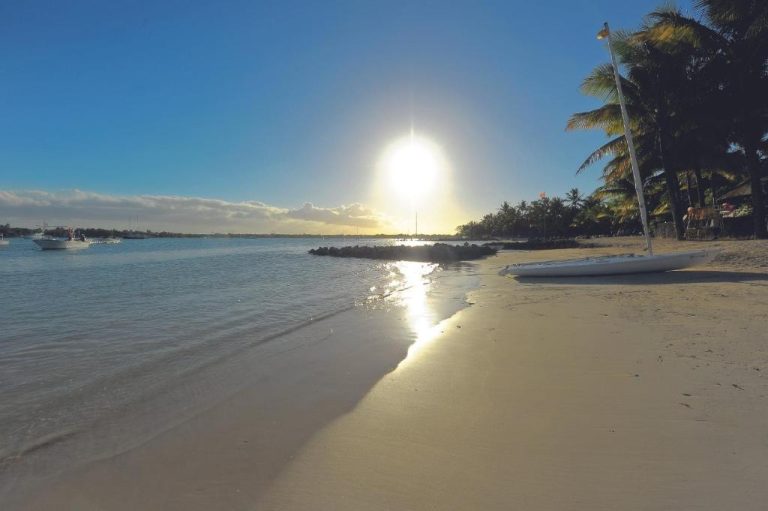 Playa de arena blanca con palmeras y aguas cristalinas al atardecer en Mauricia Beachcomber Resort & Spa
