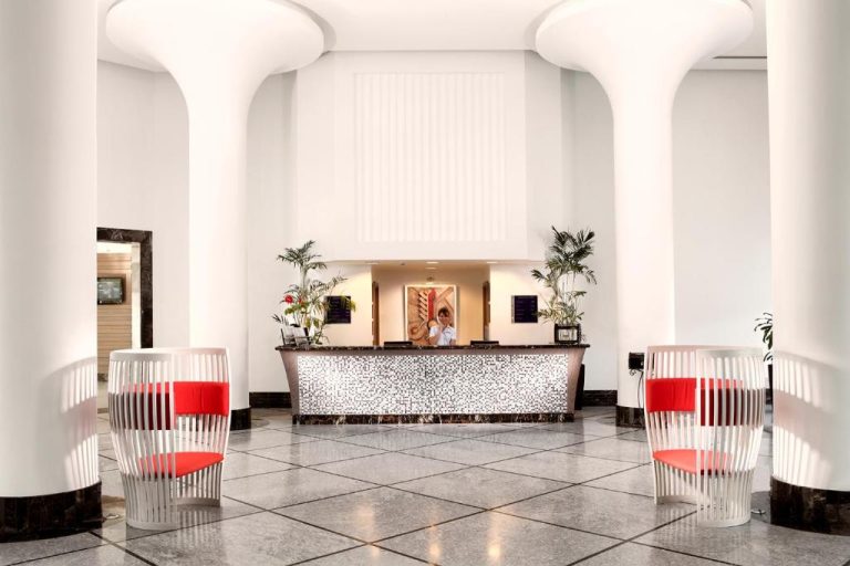 Recepción moderna del Xanadu Island con sillas rojas de diseño y columnas blancas en el lobby
