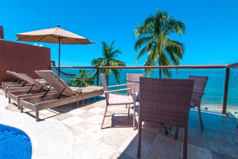 Terraza con tumbonas, mesa y sillas de ratán junto a piscina con vista al mar en Vallarta Shores Beach Hotel
