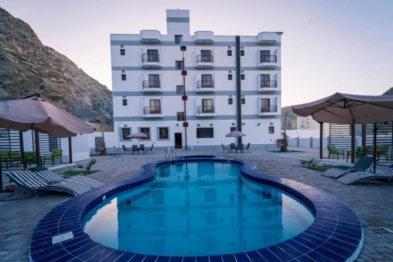 Piscina exterior con tumbonas y sombrillas del Riyam Hotel frente a imponente montaña rocosa