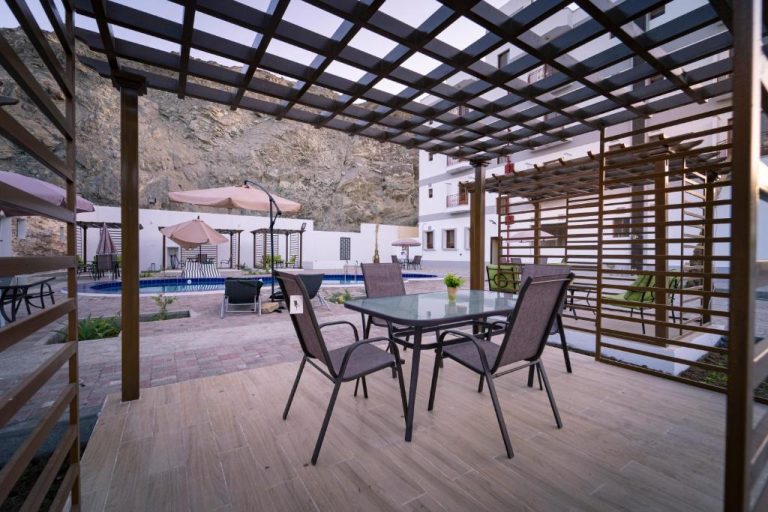 Terraza con pérgola, mesas y sillas junto a la piscina exterior del Riyam Hotel con montaña al fondo