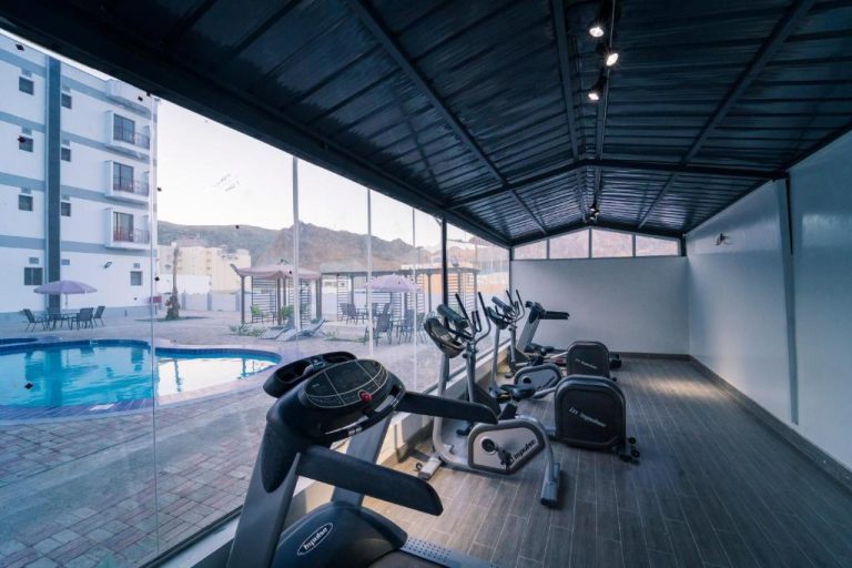 Gimnasio con equipos cardio y vistas a la piscina exterior del Riyam Hotel con montañas al fondo