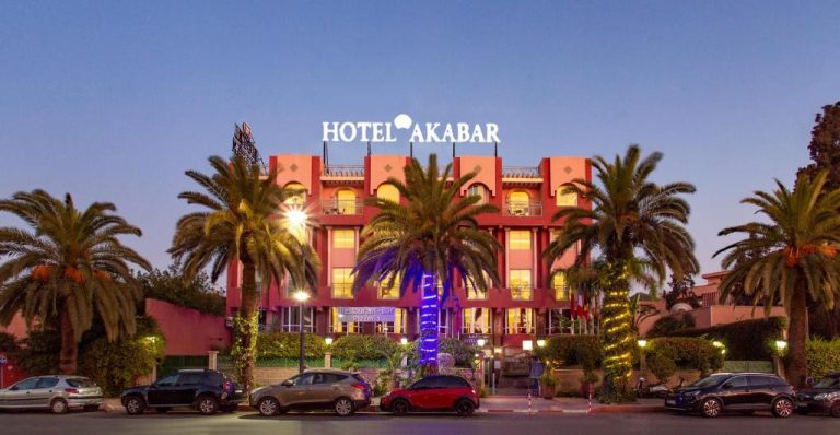 Fachada exterior iluminada del Hotel Akabar con palmeras y aparcamiento al atardecer