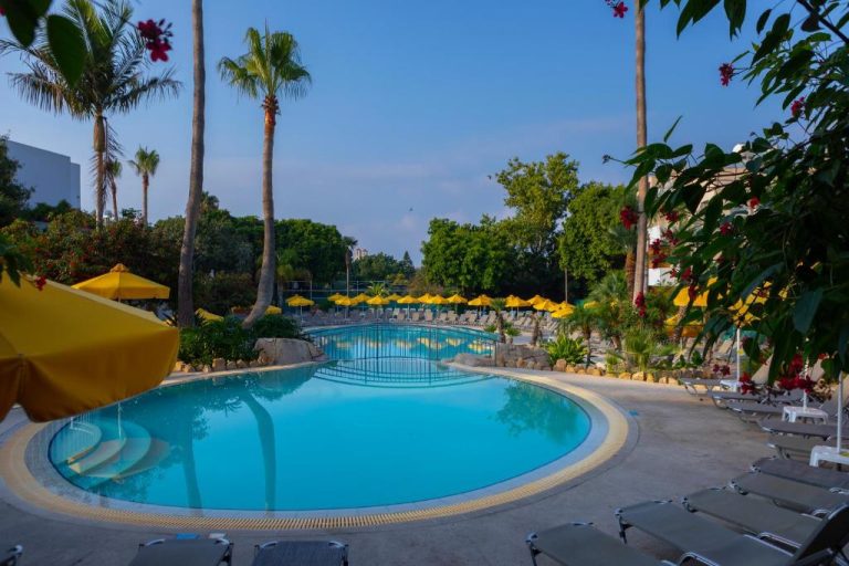 Piscina exterior con sombrillas amarillas y palmeras tropicales del Hotel Mayfair Gardens