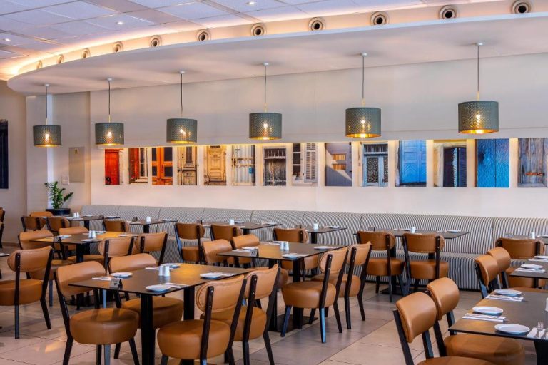 Restaurante interior del Mayfair Hotel con sillas de cuero, mesas y decoración mural de puertas coloridas