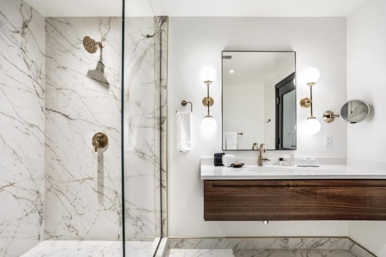 Baño de lujo con ducha de mármol blanco y griferías doradas en el Bottleworks Hotel