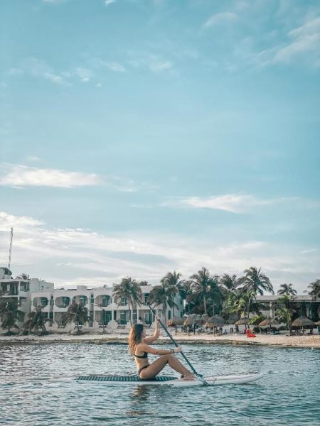 Mujer practicando paddle surf sentada en el mar frente a la playa del Paamul Hotel en México