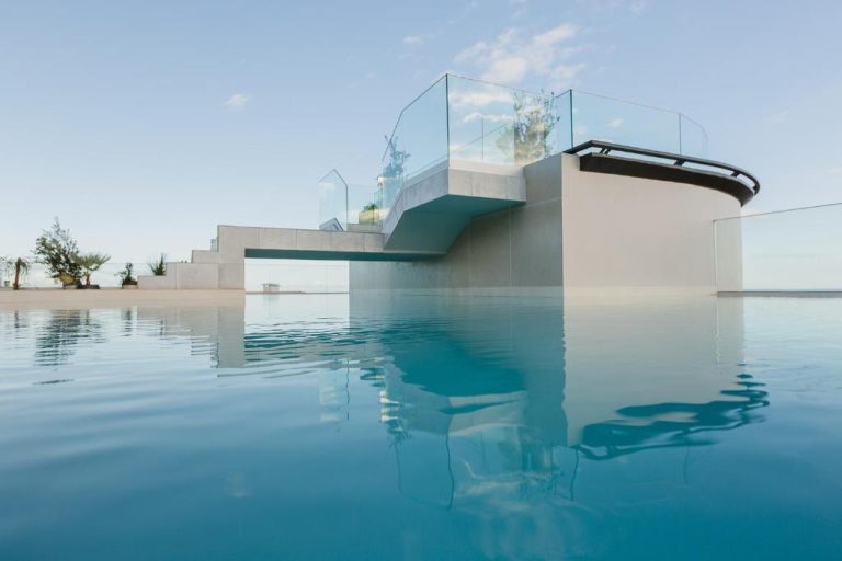Piscina infinita con terraza y barandillas de cristal del Three House Hotel al atardecer