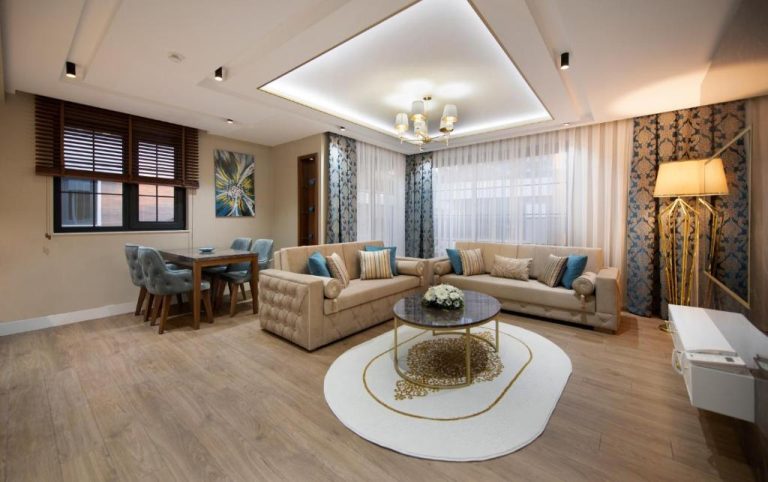 Lujoso salón con sofás beige y cojines azules en Elysium Green Suites, decoración elegante