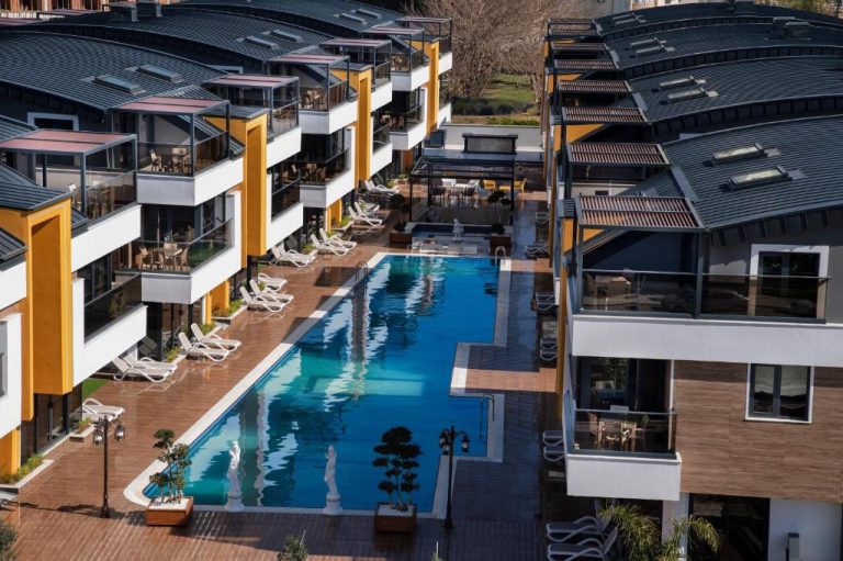 Piscina exterior rectangular con tumbonas y vistas a los edificios del Elysium Green Suites
