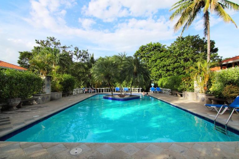 Piscina exterior de aguas turquesas rodeada de palmeras y jardín tropical en Hotel Villa del Sueño