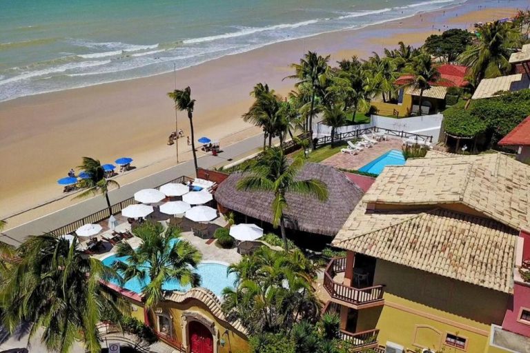 Vista aérea de la piscina exterior y playa del Manary Praia Hotel rodeado de palmeras