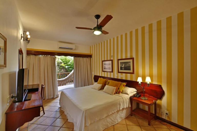 Habitación doble con pared a rayas amarillas y balcón con hamaca en Manary Praia Hotel