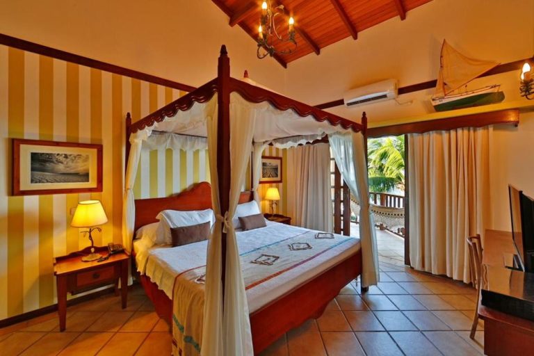 Habitación con cama de dosel y balcón con vistas tropicales en Manary Praia Hotel