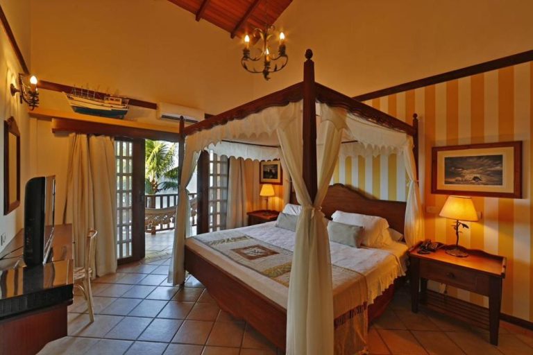 Habitación con cama de dosel de madera y decoración colonial tropical en Manary Praia Hotel