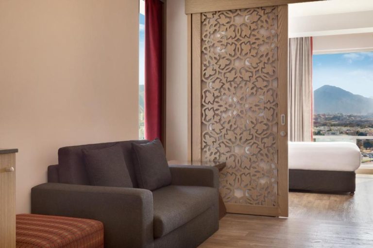 Suite con salón, biombo decorativo tallado y dormitorio con vistas a la montaña en Ramada Encore Muscat