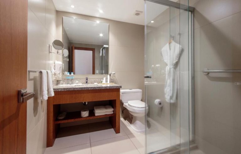 Baño completo con ducha de cristal, lavabo de granito y albornoz en el ZEN Hotel