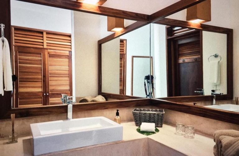 Baño elegante con lavabo rectangular y espejo de madera en Casa Altamar