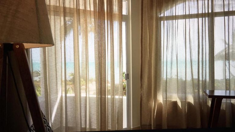 Habitación con cortinas de lino y vistas al mar turquesa y palmeras en Casa Altamar
