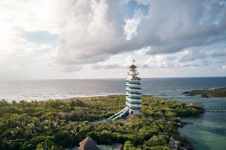 Vista aérea del faro con tobogán espiral azul del Hotel Xcaret Arte rodeado de vegetación tropical y mar