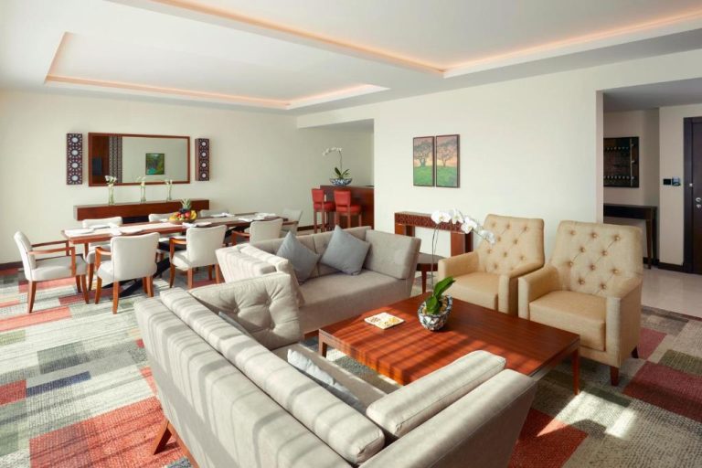Amplio salón de suite de lujo con sofás y mesa de comedor en el Royal Tulip Muscat