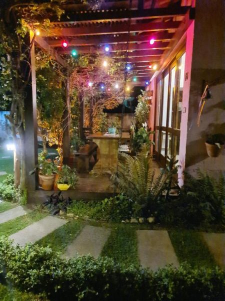 Jardim iluminado com luzes coloridas e vegetação exuberante na Pousada Vila Rosada à noite